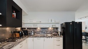 A modern kitchen with a gas stove, black refrigerator, and white cabinets. - Amsterdam Group Villa | 20+ | Spa | Karaoke (Zwanenburg)