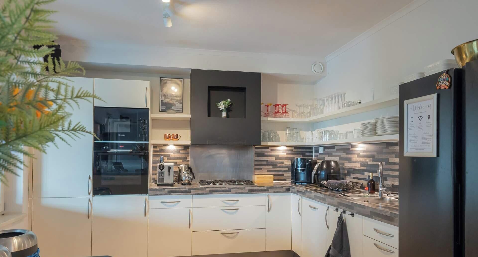 A modern kitchen with white cabinets, a Bosch oven, a coffee machine, and a black refrigerator.