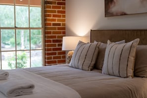 Ein Hotelzimmer mit Bett, Kissen, einer Lampe und einem Fenster mit Blick auf Grünflächen.