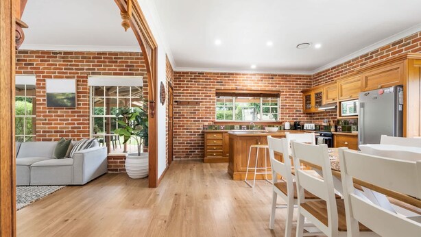 A kitchen with brick walls, wooden cabinets, a central island, and a dining area with white chairs. - 6 Minutes from Bathurst CBD - The Estait Homestead - Laffing Waters Retreat (Laffing Waters)