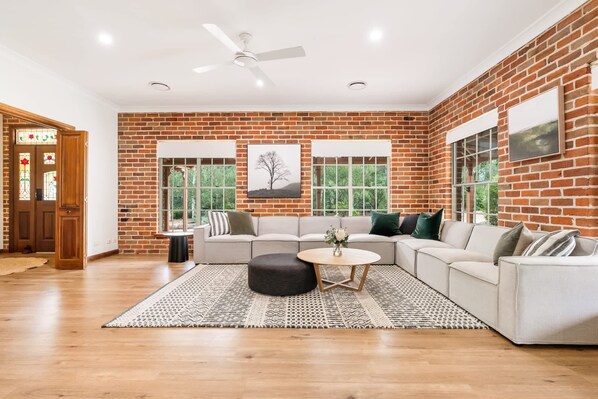 A spacious living room with a brick wall, large windows, a ceiling fan, and a sectional sofa.