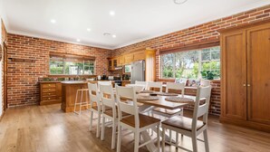 A kitchen with a brick wall, wooden cabinets, a dining table with chairs, and a large window. - 6 Minutes from Bathurst CBD - The Estait Homestead - Laffing Waters Retreat (Laffing Waters)