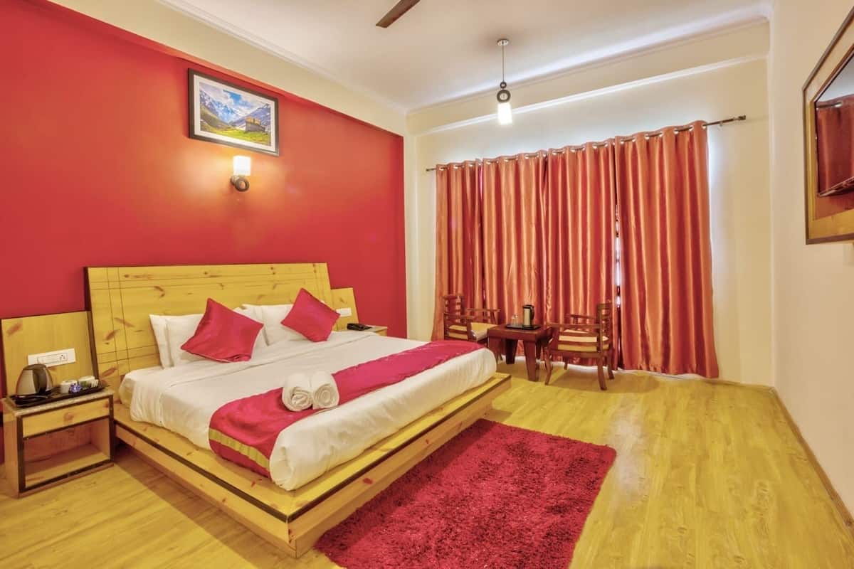 A hotel room with a wooden bed, red walls, a red carpet, a small table with chairs, and a window with curtains.