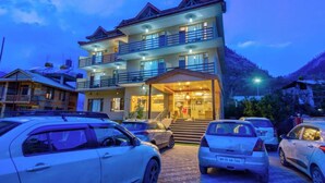 A multi-story hotel with a central entrance, balconies, and a parking area with cars. - Hotel Grand Oasis (Manali)