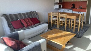 A compact living space with a sofa, a wooden dining table, and a kitchenette.