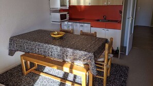 A compact kitchen with a microwave, oven, and sink. There's a dining table with chairs and a bench.