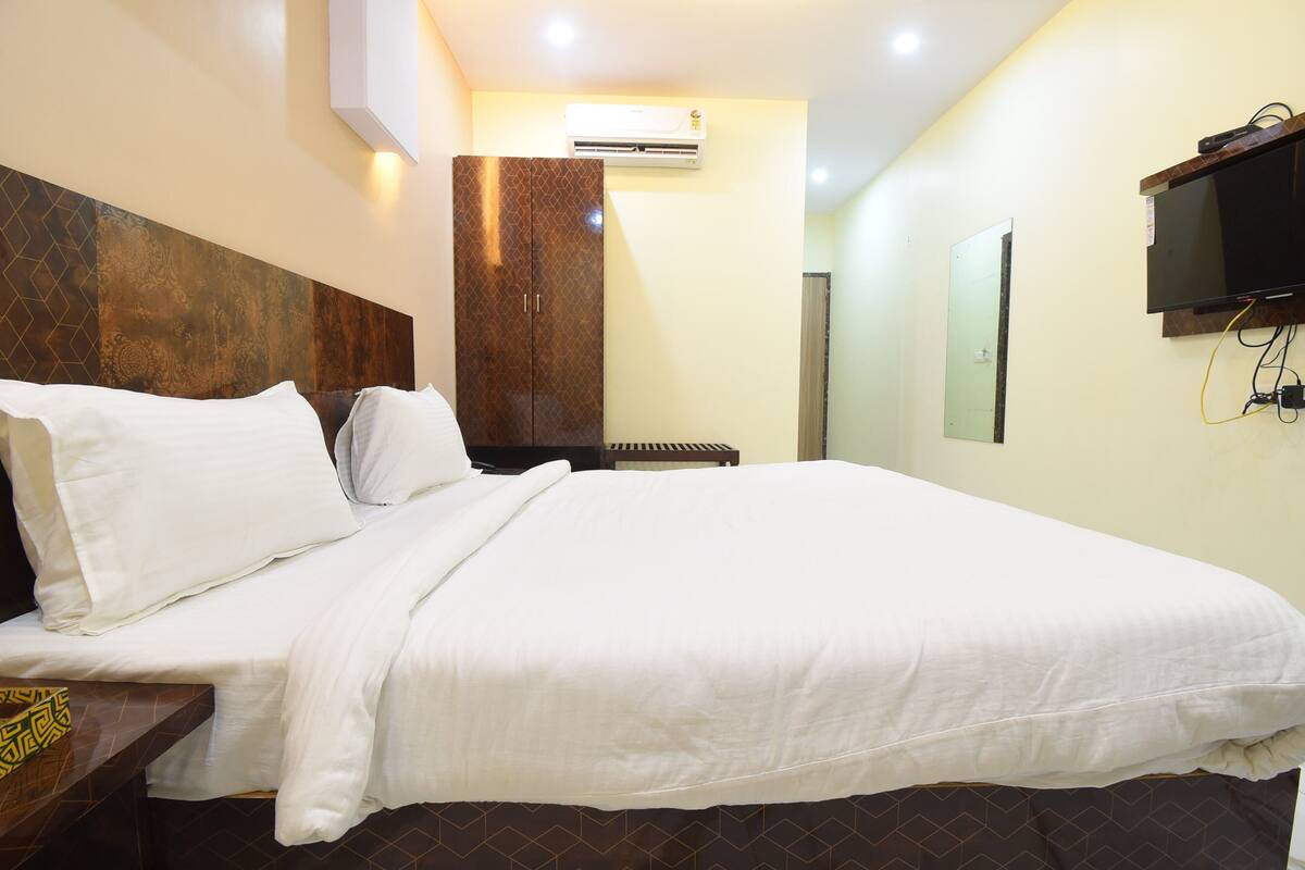 A hotel room with a large bed, a wardrobe, an air conditioning unit, a television, and a mirror.