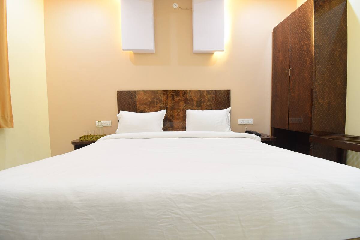 A hotel room with a large bed, a wooden headboard, two bedside tables, and a wardrobe.