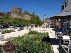 A street with parked cars, a restaurant with outdoor seating, and a historic building with a tower.