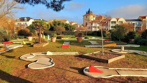 Um jardim com paisagismo, caminhos sinuosos, vasos de plantas e um edifício com varandas ao fundo.