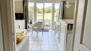 A room with a sofa, a TV, a dining area with chairs, and a view through a glass door to an outdoor space. - Moulin Vert, village house with swimming pool (Talmont-Saint-Hilaire)