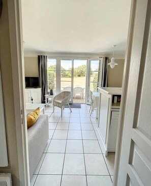 A room with a sofa, a TV, a dining area with chairs, and a view through a glass door to an outdoor space.