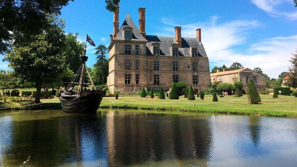 A historic building with a large courtyard, a body of water, and a sailing ship.