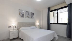 Une chambre à coucher avec un lit, des tables de chevet, une fenêtre avec des rideaux et des œuvres d’art murales.