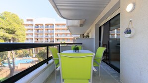 Un balcon avec une table et des chaises, donnant sur la piscine, et un bâtiment visible au loin.