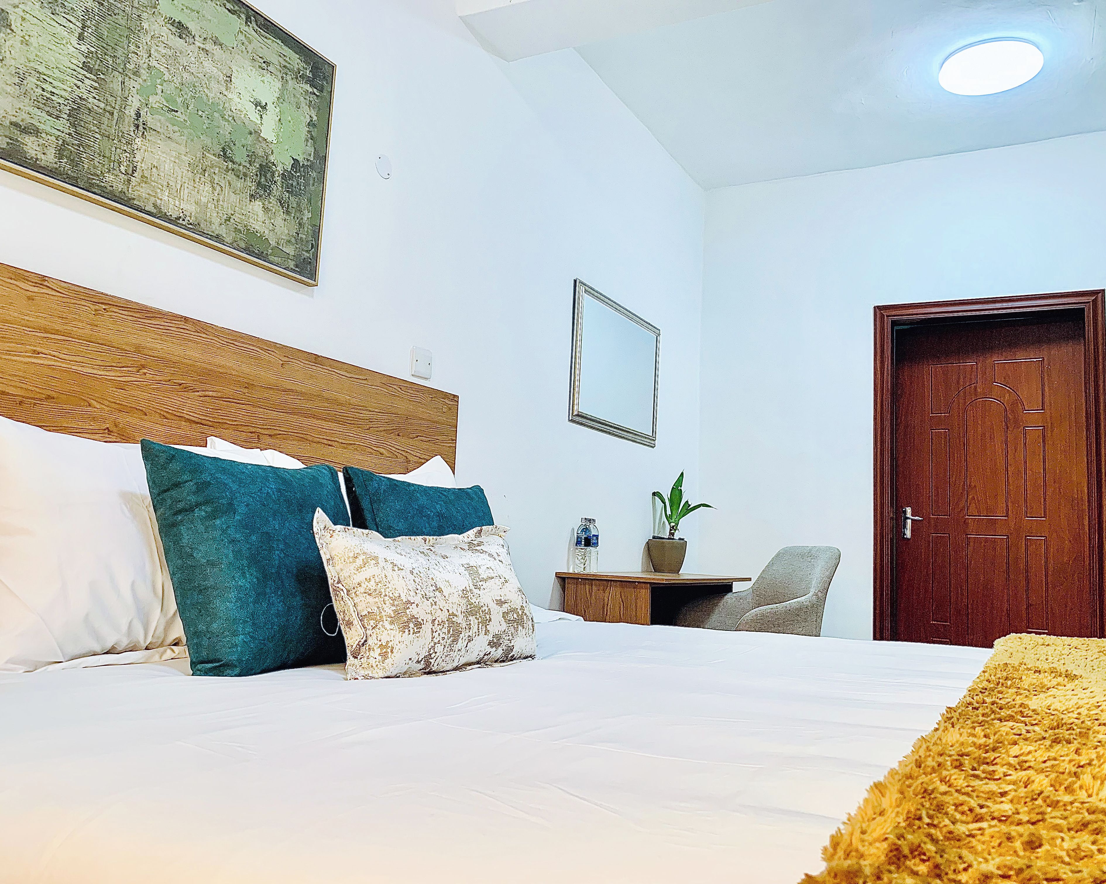 Une chambre à coucher avec un lit, des oreillers, une table de chevet, une chaise, une porte en bois et un luminaire au plafond.