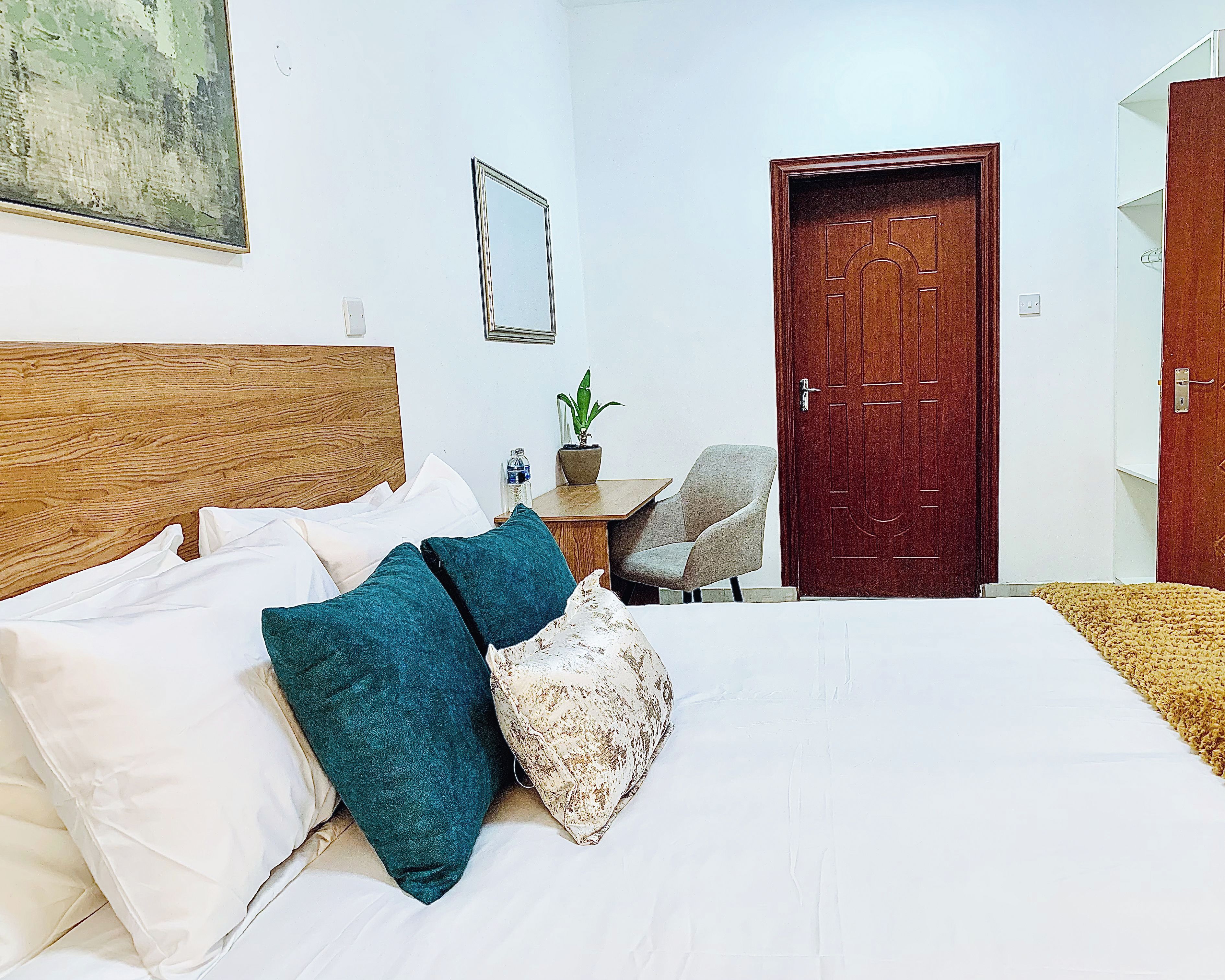 Une chambre d’hôtel avec un lit, des oreillers, une petite table avec une plante, une chaise et une porte.