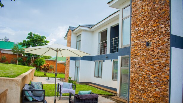 Una casa moderna con un muro de piedra, un patio con muebles de exterior y un paraguas grande.