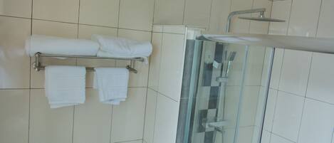 A bathroom with a glass-enclosed shower, a towel rack with neatly folded towels, and a tiled floor.