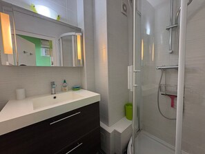 Ein Badezimmer mit einem weißen Waschbecken, dunklen Schränken, einer Glasdusche und einem Spiegel an einer Wand in Grünton.