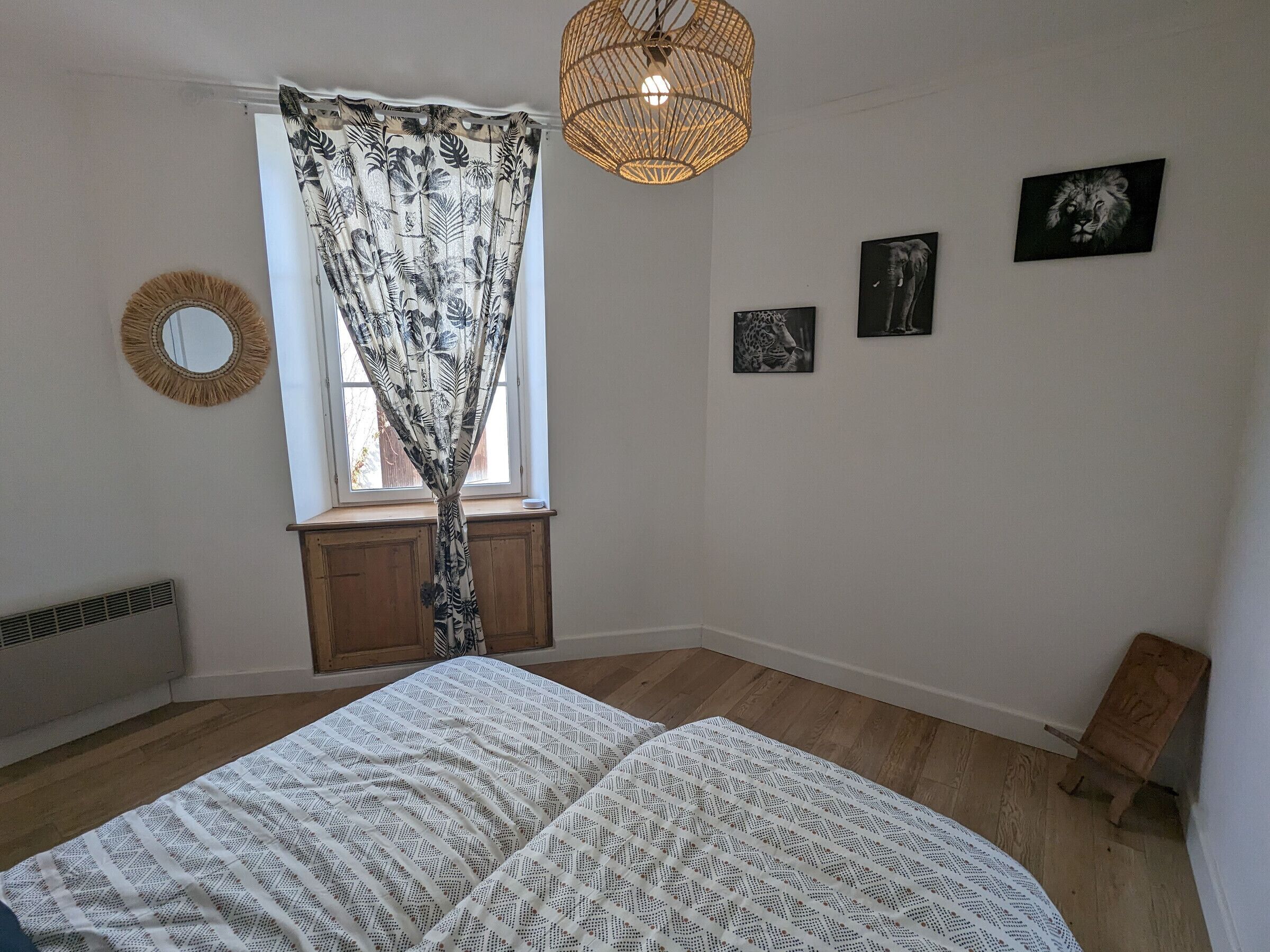 Een slaapkamer met een bed, een raam met gordijnen, een spiegel aan de muur en drie ingekaderde foto's.