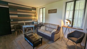 A living room with a sofa, armchairs, a coffee table, a desk, and a wall with horizontal wooden planks.