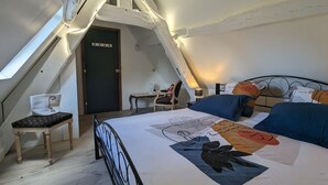A bedroom with a sloped ceiling, a bed with patterned bedding, a chair, and a desk.