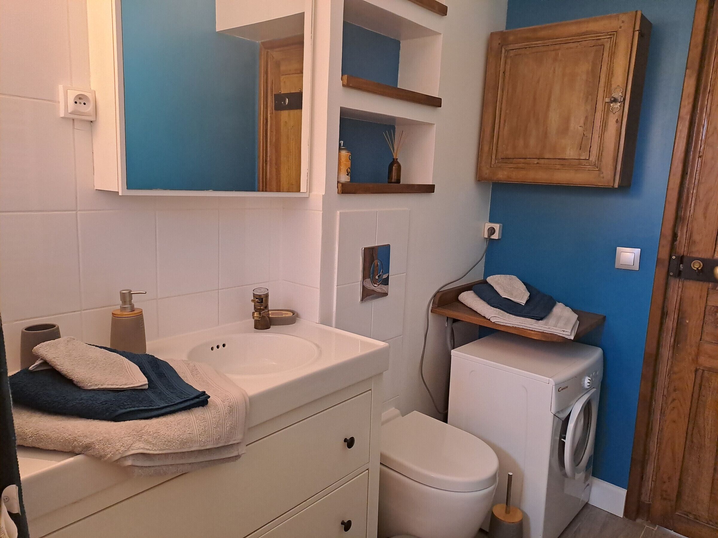 A bathroom with a sink, mirror, towel rack, toilet, and washing machine.