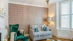 A living room with a fireplace, a green armchair, a grey sofa, and a round coffee table. - Beautiful Cottage in Central Whitstable (Whitstable)