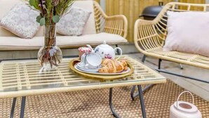 A glass-top table with a tea set and pastries, wicker chairs, and a sofa with cushions. - Beautiful Cottage in Central Whitstable (Whitstable)