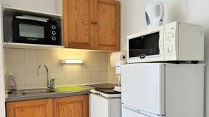 A compact kitchenette with a black microwave, a white microwave, a sink, and a refrigerator.