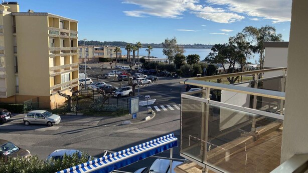 Vista de un estacionamiento con varios automóviles, un paso de peatones y un edificio con balcones que dan a una masa de agua.