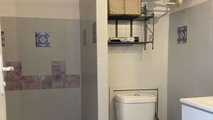 Un baño con ducha, inodoro y un estante con artículos de aseo.