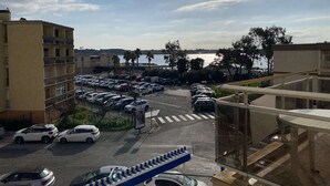 Un estacionamiento con varios coches, un paso de peatones y una vista de un cuerpo de agua con palmeras al fondo.