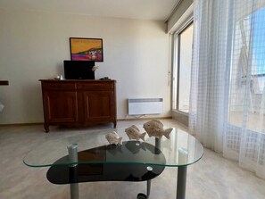 A room with a glass-top table, wooden cabinet, and a poster on the wall. - Renovated studio with sea view, beach access, and private parking (Saint-Jean-de-Monts)