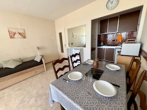 A dining area with a table set for four, a sofa, and a kitchen in the background. - Renovated studio with sea view, beach access, and private parking (Saint-Jean-de-Monts)