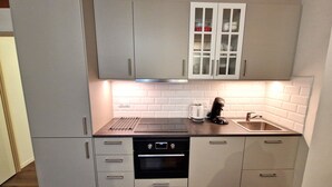 Une cuisine compacte avec des meubles gris, un four encastré, un lave-vaisselle, une bouilloire et un évier.