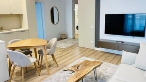 A modern living room with a TV, a wooden coffee table, a sofa, and a dining area with chairs. - Joy City Stay Vivalia 7B-26 (Timișoara)