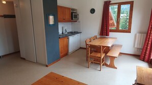 Una cocina compacta con comedor, armarios de madera y una ventana con cortinas.