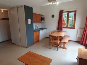 Una cocina compacta con comedor, armarios de madera y una ventana con cortinas.