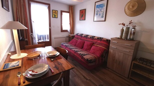 Una sala de estar acogedora con una mesa de comedor de madera, un sofá, una lámpara y un sombrero colgado en la pared.