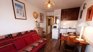 Un espacio habitable compacto con sofá, mesa de comedor, zona de cocina y un refrigerador pequeño.