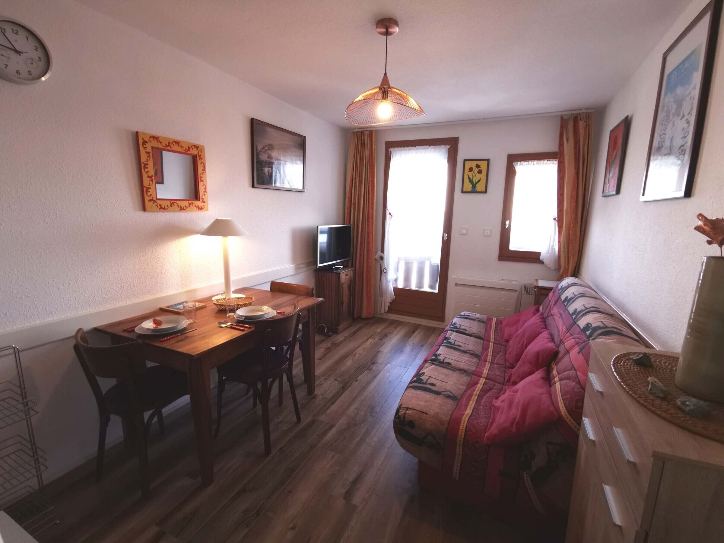 A cozy living room with a wooden dining table, a sofa, a TV, and a window with curtains.