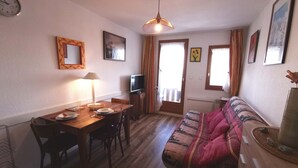 Una sala de estar acogedora con una mesa de comedor de madera, un sofá, un televisor y una ventana con cortinas.