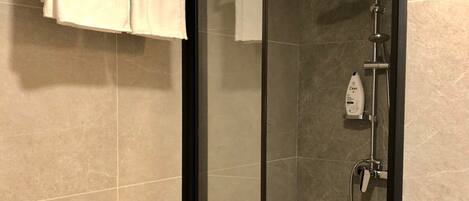 A modern bathroom with a glass-enclosed shower, a towel rack with two towels, and a bottle of Dove soap.