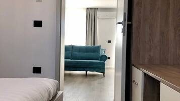 Een slaapkamer met een bed, een kledingkast en uitzicht op een andere kamer met een bank.