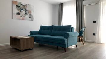 Een woonkamer met een smaragdgroene bank, een houten salontafel en een modern abstract schilderij aan de muur.