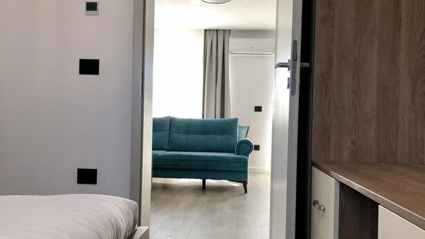 Ett modernt sovrum med en säng, en garderob och en turkosfärgad soffa i det intilliggande rummet.