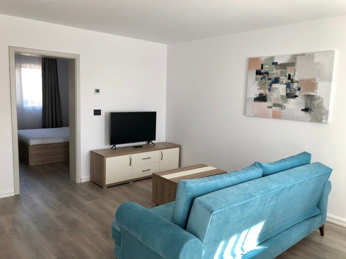 Ein modernes Wohnzimmer mit einer Couch, einem Fernseher auf einer Holzkommode und einem Bild an der Wand.