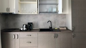 Ett modernt kök med ljusa träskåp, en svart bänkskiva, en kaffebryggare och ett handfat.
